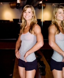 Verity Somers, founder of Raw Workouts, a blonde woman wearing workout clothes and standing next to a large mirror