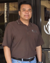 Mario, a slightly smiling man in a brown polo shirt, stands in front of his business's door.
