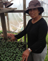 Muy, a smiling woman wearing a purple hat, stands in a greenhouse.