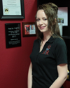 Rebekah, a smiling woman in a black polo shirt, stands in front of her massage awards.