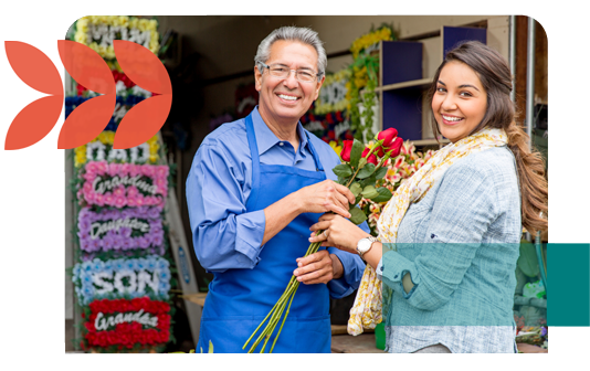 A flower shop owner and a customer smile at the storefront